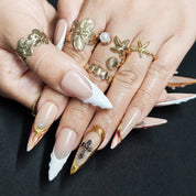 Close-up of Divine Gold handmade press-on nails showing 3D milky white embossed details, gold cross embellishments, and watercolor nail art
