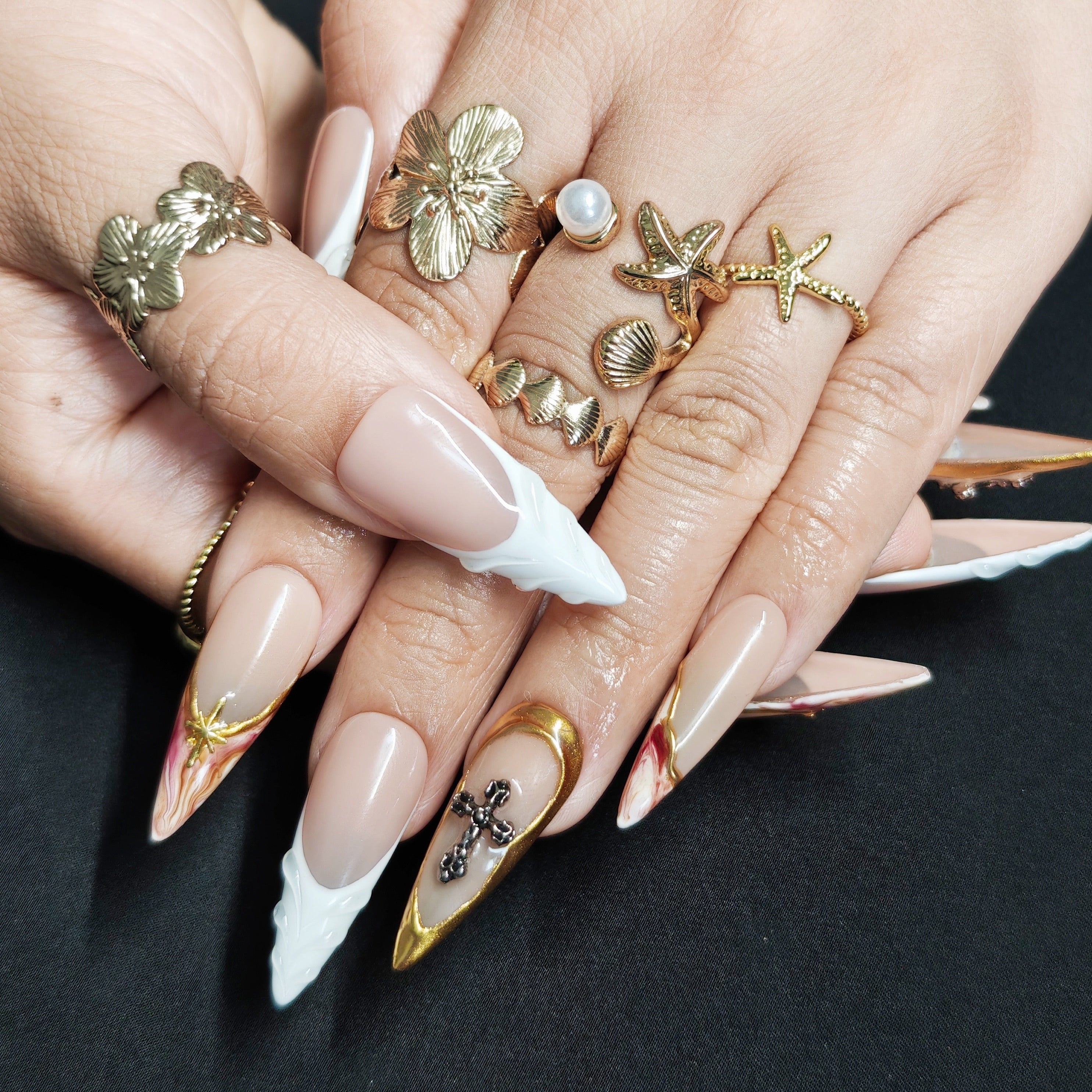 Close-up of Divine Gold handmade press-on nails showing 3D milky white embossed details, gold cross embellishments, and watercolor nail art