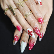 White and red almond press-on nails with 3D floral designs, rhinestones, pearls, and gold bead accents for a luxurious handmade look.