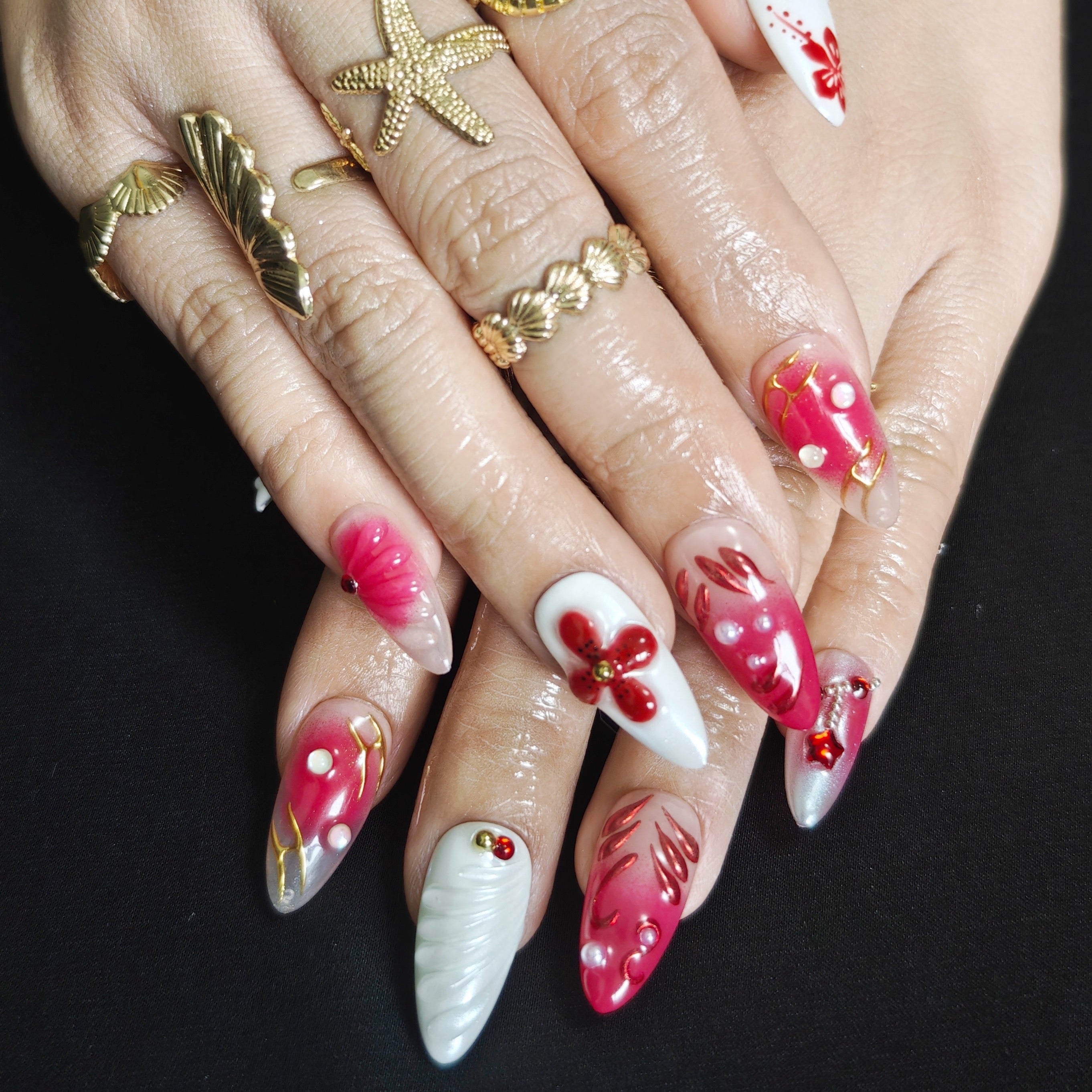 White and red almond press-on nails with 3D floral designs, rhinestones, pearls, and gold bead accents for a luxurious handmade look.