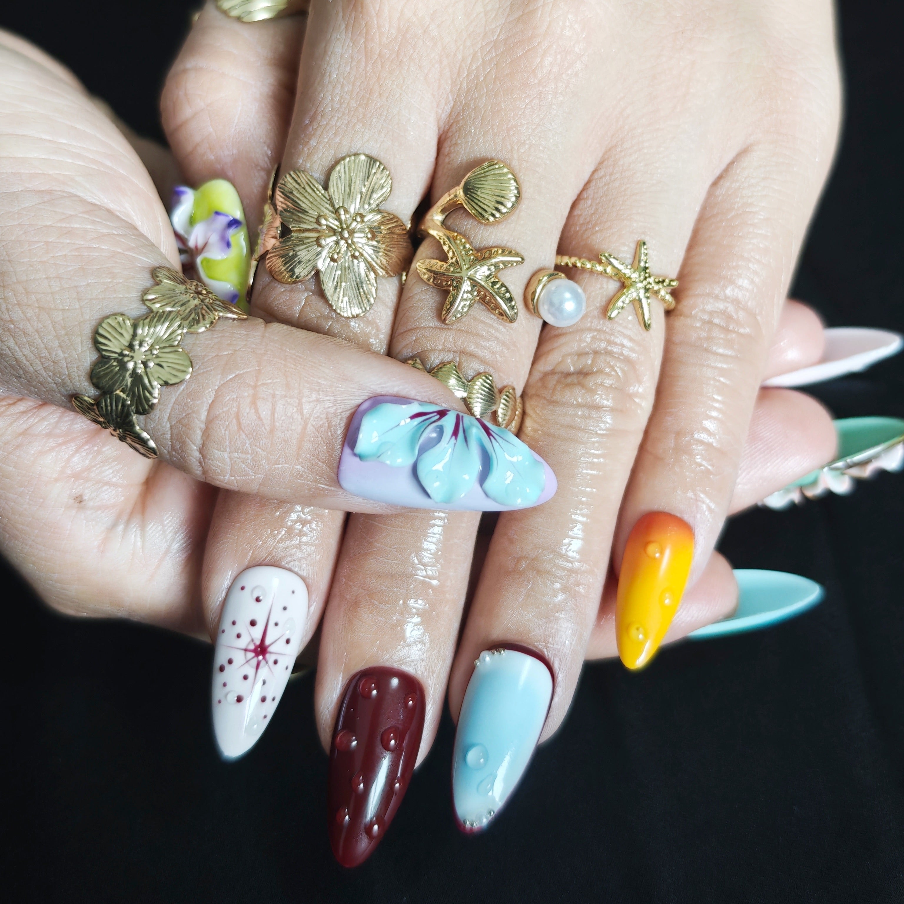 Almond press-on nails with three vivid purple 3D flowers and a blue, green, purple gradient design.
