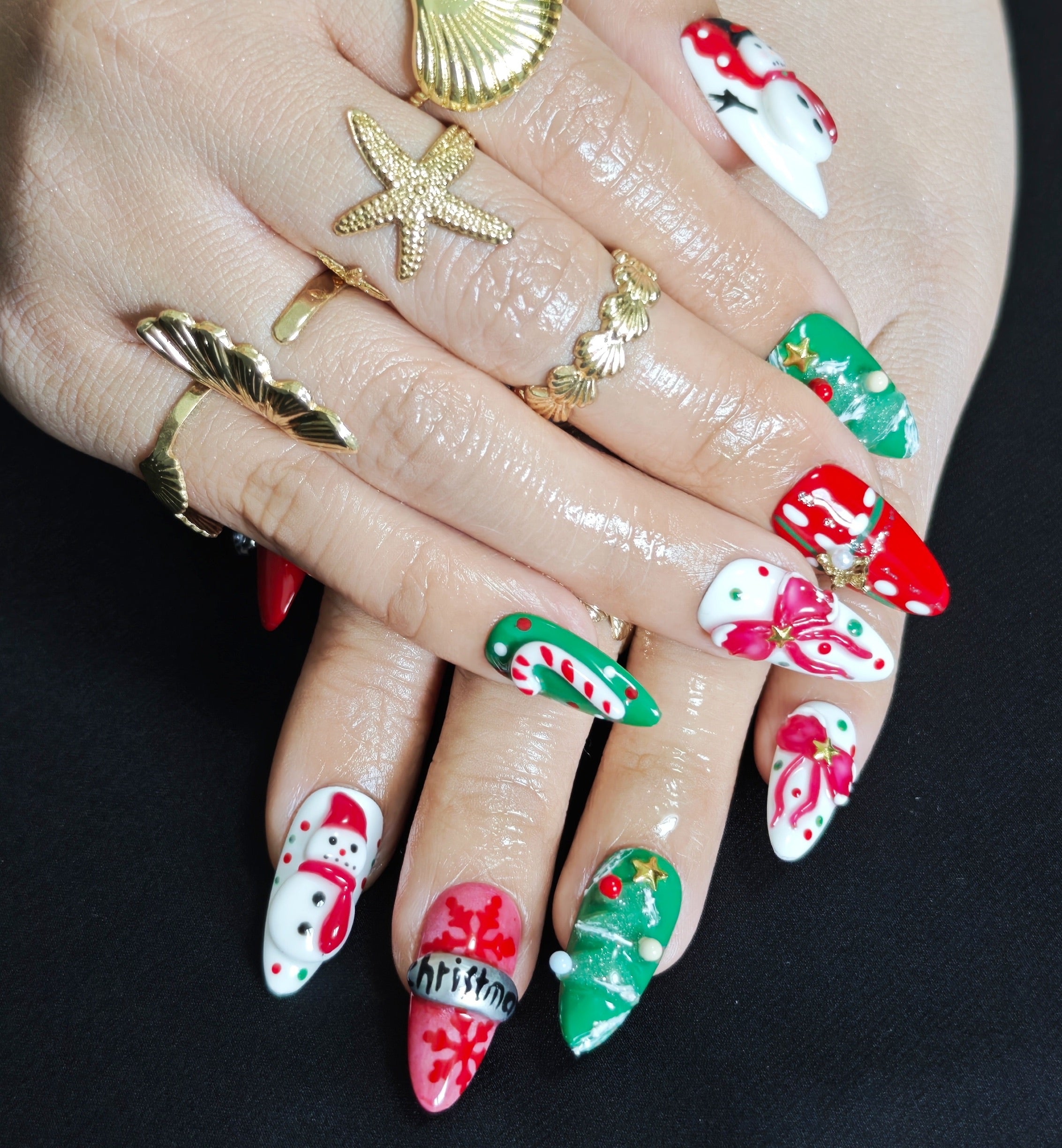 Almond press-on nails with two 3D snowmen, a Christmas tree, and bow in red, green, and white for festive holiday look.