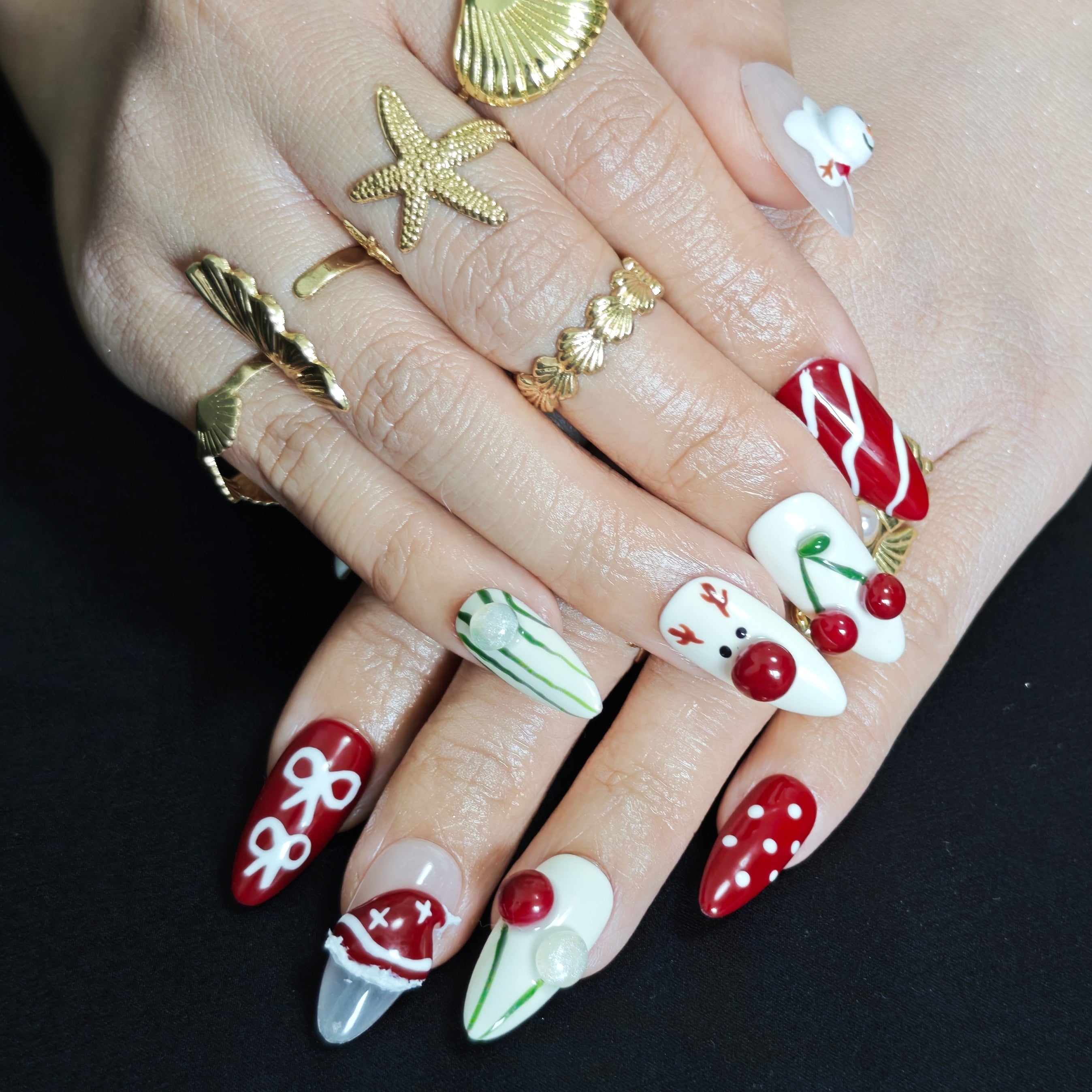 Red and white almond press-on nails with 3D snowman, cherry, Santa hat, bow, and reindeer designs for festive Christmas style.