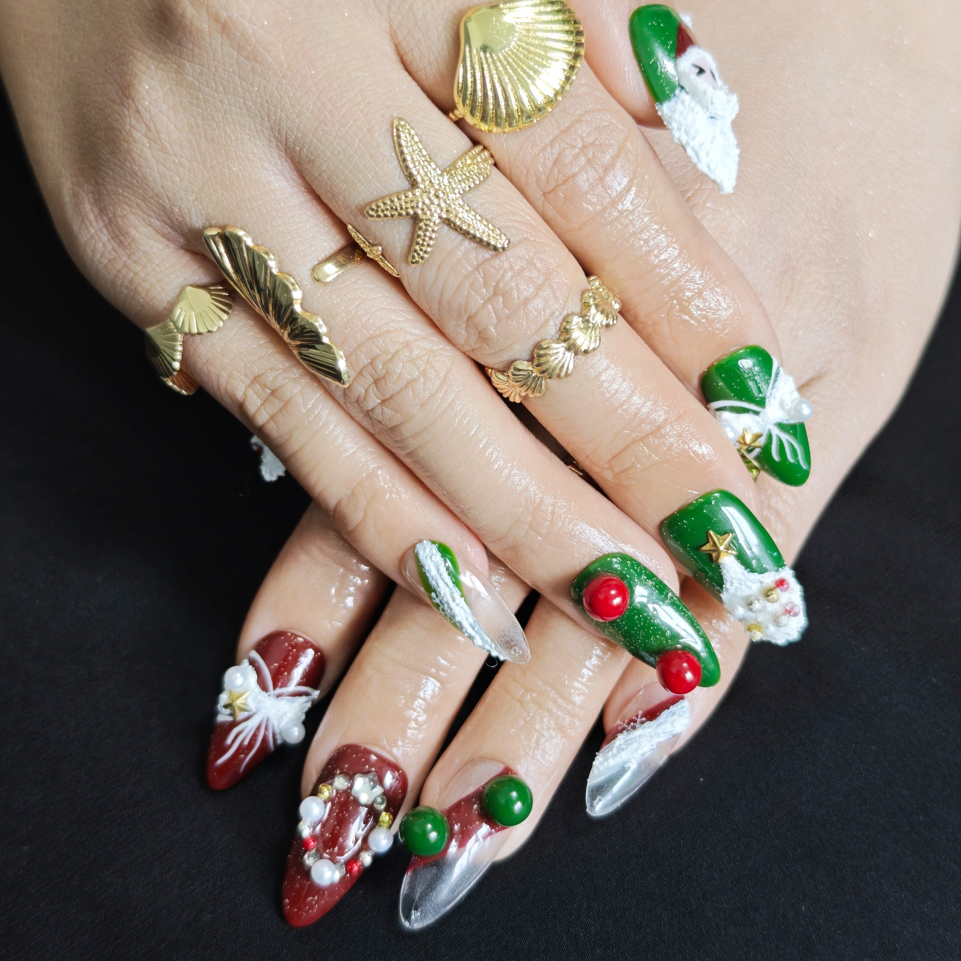 Red and green almond press-on nails with 3D Santa, Christmas tree, and wreath designs for festive holiday style.