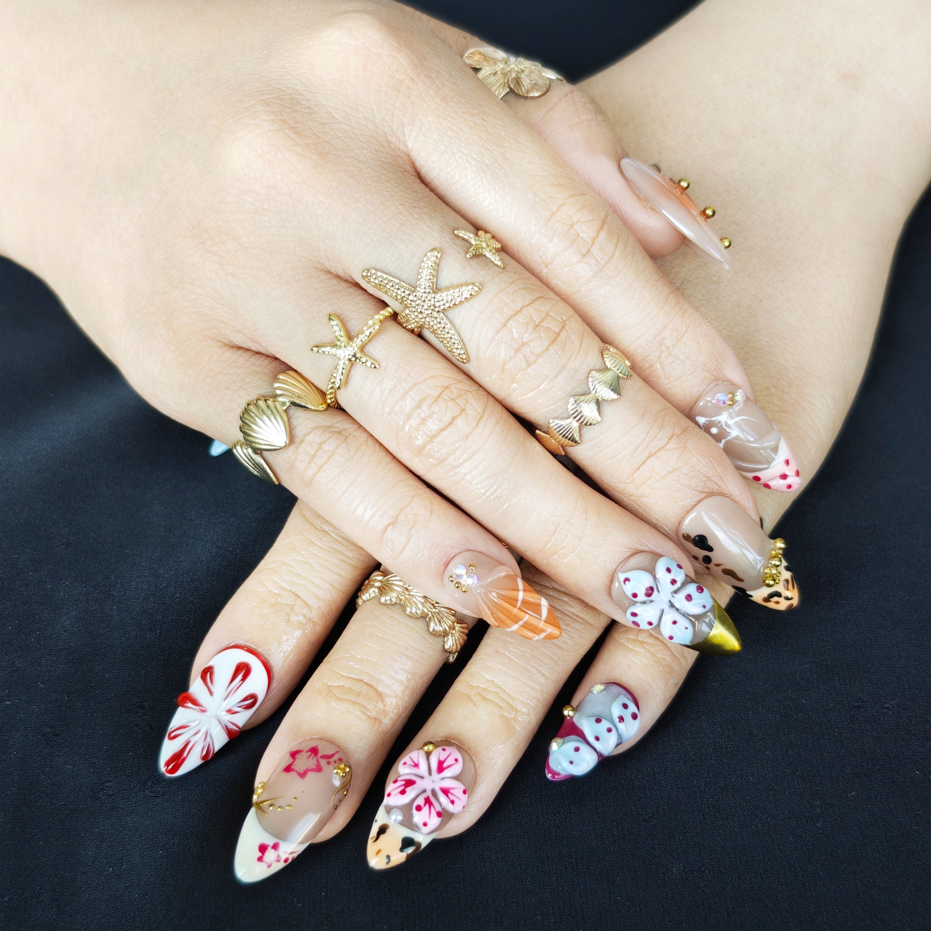 Woman wearing Flora Island 3D orange almond press-on nails with tropical colors, floral details, and elegant vacation manicure style