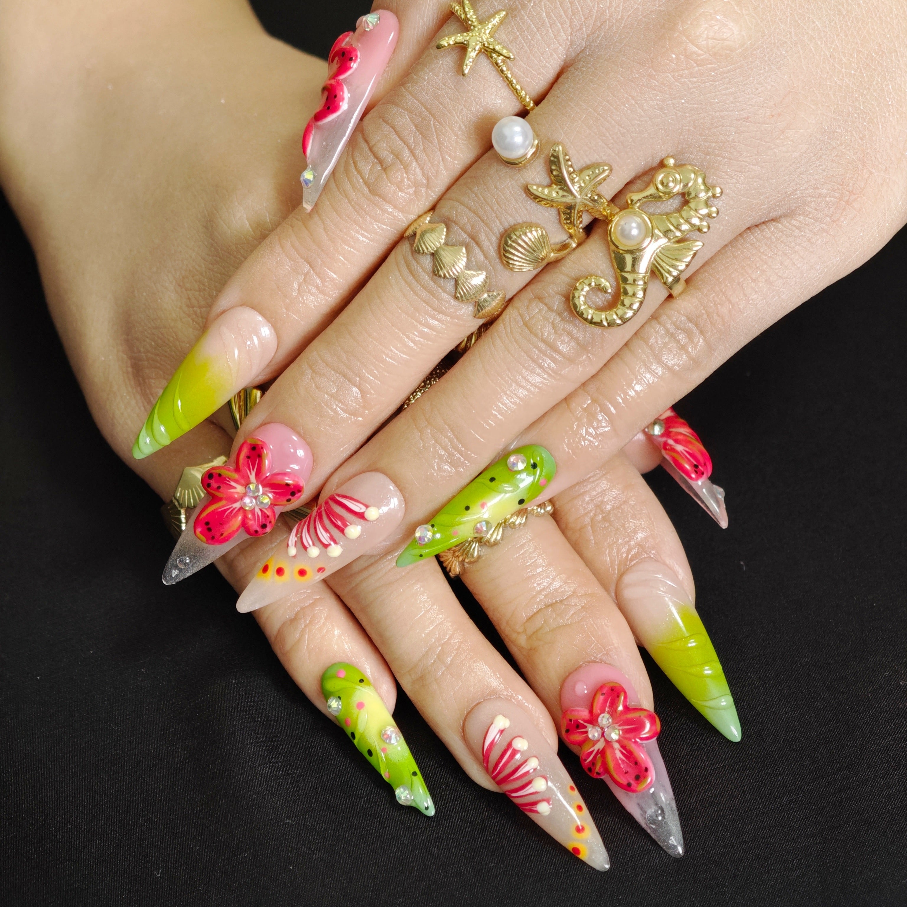 Stiletto press-on nails with four large red tropical 3D flowers, green accents, and multiple sparkling rhinestones.