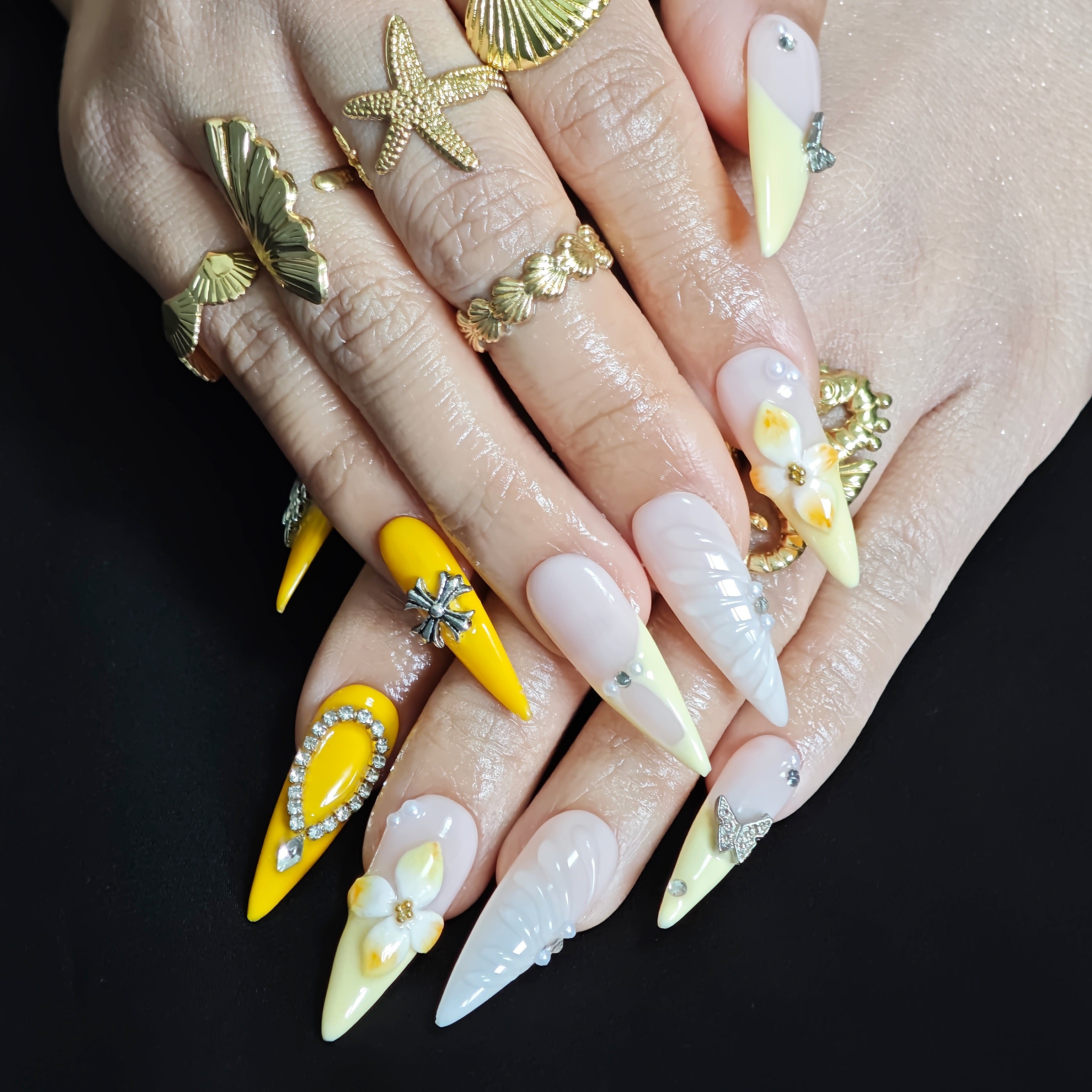 Woman wearing Marigold Rebel stiletto press-on nails with bright yellow tones, 3D floral details, silver accessories, and bold summer manicure style