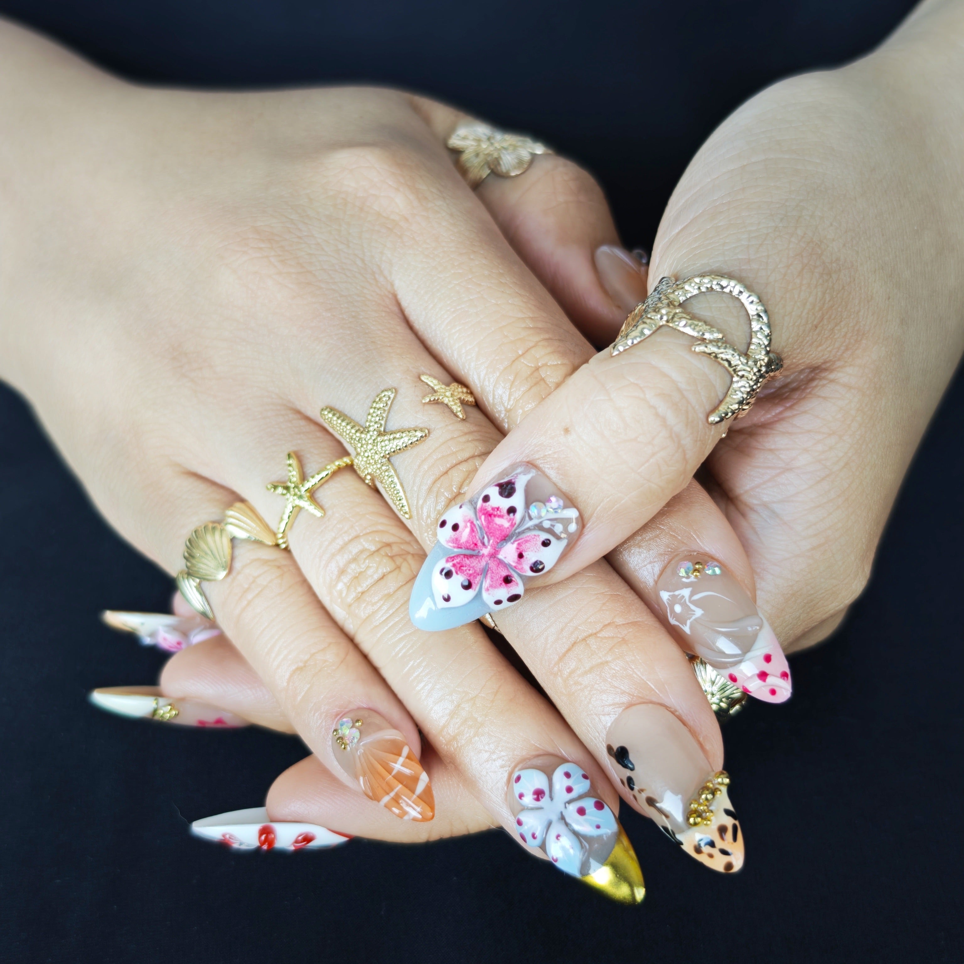 Close-up of Flora Island handmade press-on nails showing realistic 3D orange details, sculpted flowers, gold accents, and French nail art design