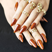 Almond-shaped press-on nails with caramel ombre and subtle snake pattern for minimalist luxury style.