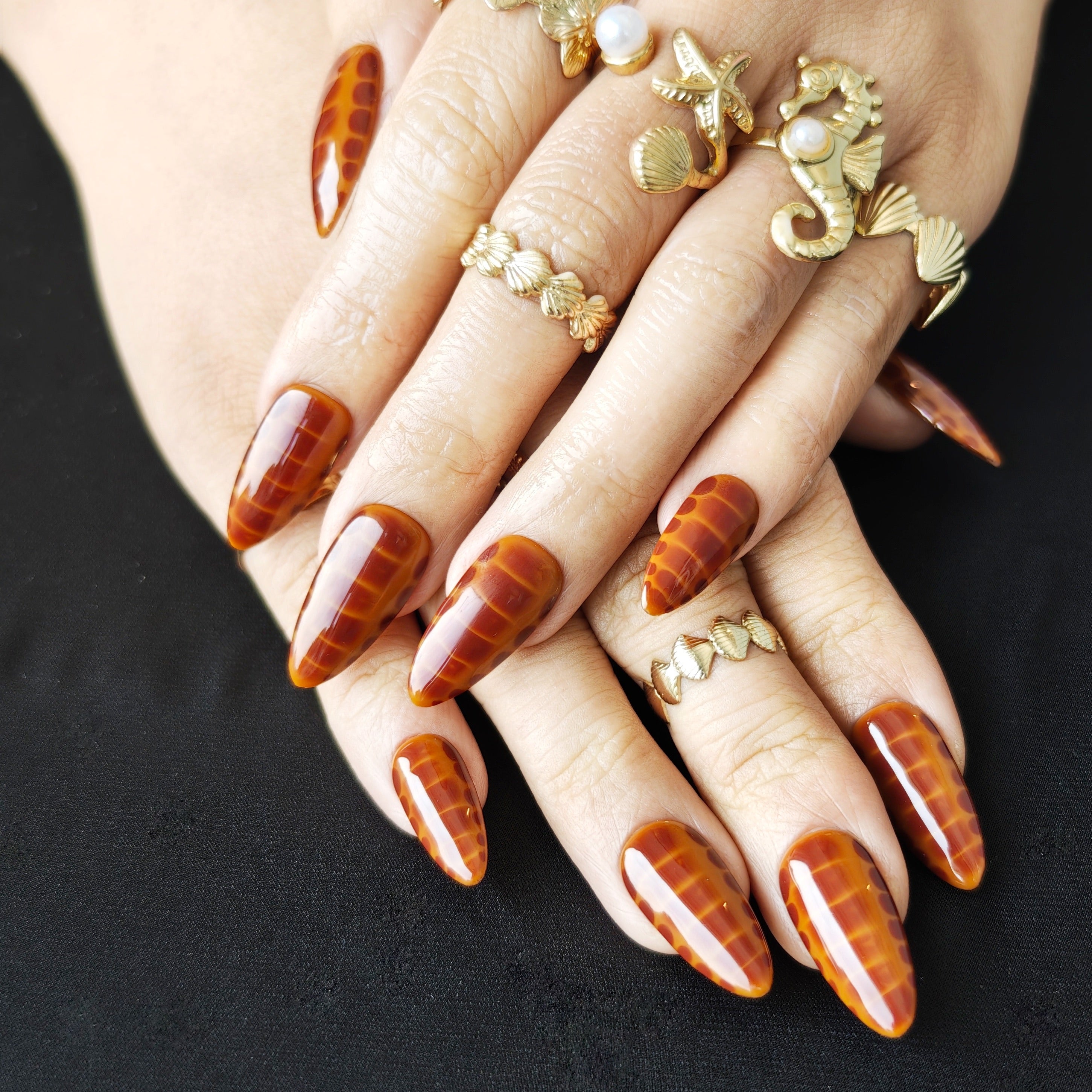 Almond-shaped press-on nails with caramel ombre and subtle snake pattern for minimalist luxury style.