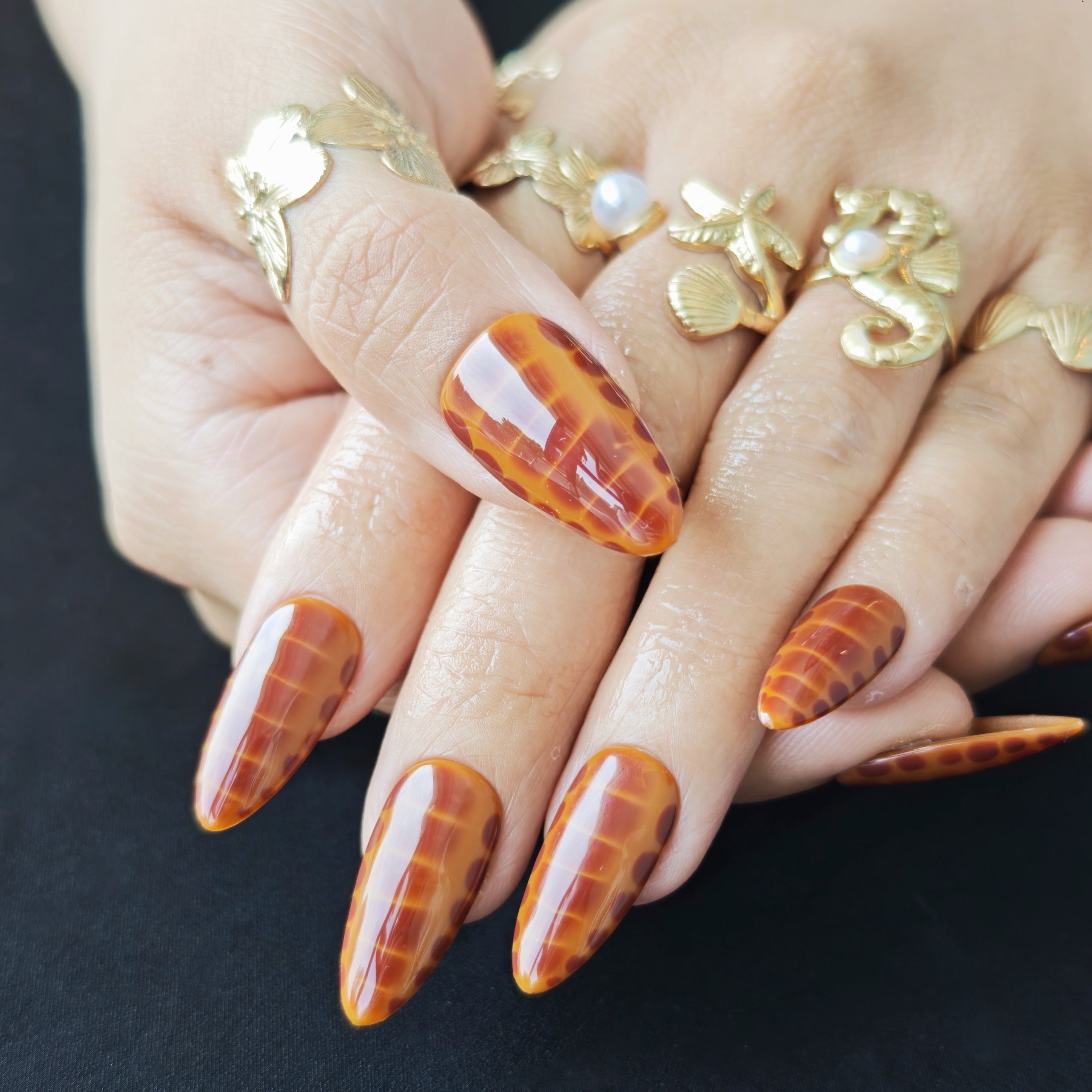 Almond-shaped press-on nails with caramel ombre and subtle snake pattern for minimalist luxury style.