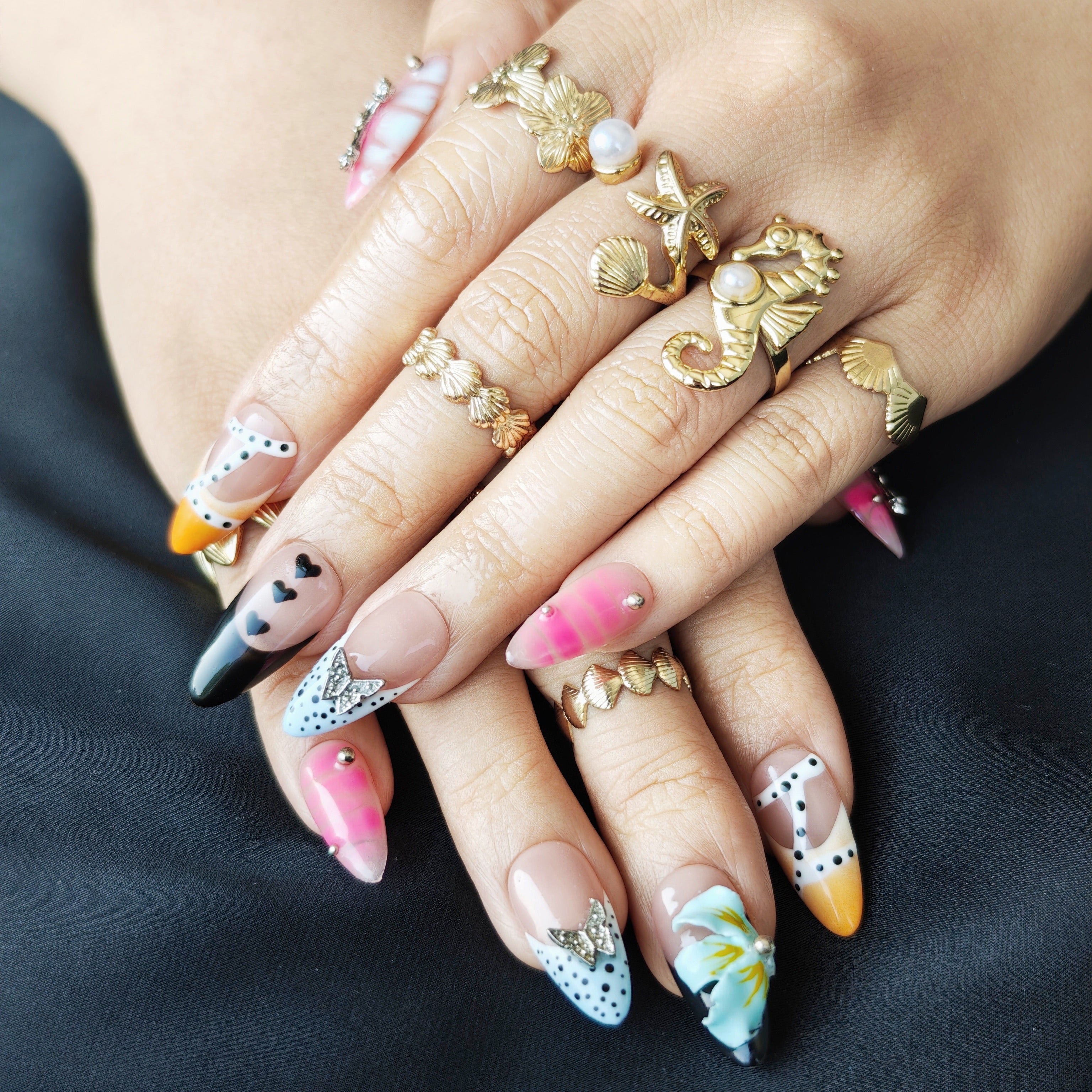Almond press-on nails in yellow with pink cross, blue floral accents, and silver butterfly decorations.
