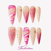 Pink Riot stiletto press-on nails featuring pink marble fluid design, white bow details, crystal accents, and handmade luxury nail art