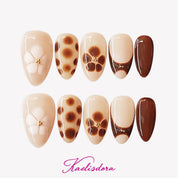 Mocha and brown short almond French press-on nails with white floral accents, designed for a cozy winter aesthetic.