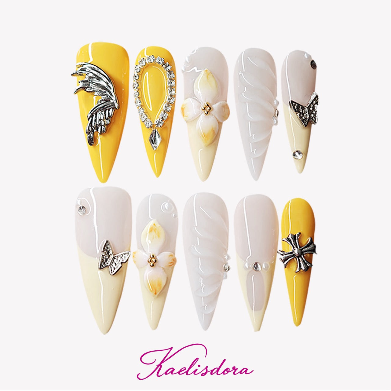 Marigold Rebel yellow stiletto press-on nails featuring 3D white flowers, silver bow charms, nude pink gradient, and luxury handmade nail art