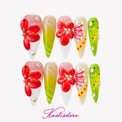 Stiletto press-on nails with four large red tropical 3D flowers, green accents, and multiple sparkling rhinestones.